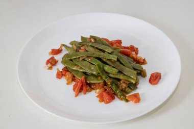 Domates ve soğanlı kızarmış yeşil fasulye. Yemekte fasulyeli lezzetli yemek ya da beyaz tabakta öğle yemeği.