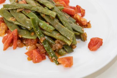 Domates ve soğanlı kızarmış yeşil fasulye. Yemekte fasulyeli lezzetli yemek ya da beyaz tabakta öğle yemeği.