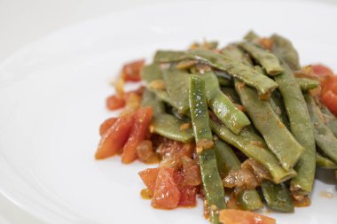 Domates ve soğanlı kızarmış yeşil fasulye. Yemekte fasulyeli lezzetli yemek ya da beyaz tabakta öğle yemeği.
