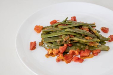 Domates ve soğanlı kızarmış yeşil fasulye. Yemekte fasulyeli lezzetli yemek ya da beyaz tabakta öğle yemeği.