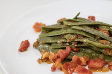 Domates ve soğanlı kızarmış yeşil fasulye. Yemekte fasulyeli lezzetli yemek ya da beyaz tabakta öğle yemeği.
