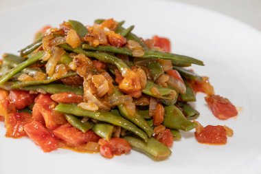 Domates ve soğanlı kızarmış yeşil fasulye. Yemekte fasulyeli lezzetli yemek ya da beyaz tabakta öğle yemeği.