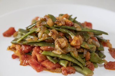 Domates ve soğanlı kızarmış yeşil fasulye. Yemekte fasulyeli lezzetli yemek ya da beyaz tabakta öğle yemeği.