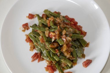 Domates ve soğanlı kızarmış yeşil fasulye. Yemekte fasulyeli lezzetli yemek ya da beyaz tabakta öğle yemeği.