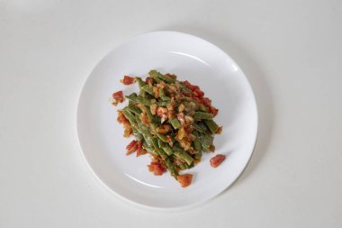 Domates ve soğanlı kızarmış yeşil fasulye. Yemekte fasulyeli lezzetli yemek ya da beyaz tabakta öğle yemeği.