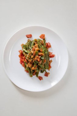 Domates ve soğanlı kızarmış yeşil fasulye. Yemekte fasulyeli lezzetli yemek ya da beyaz tabakta öğle yemeği.