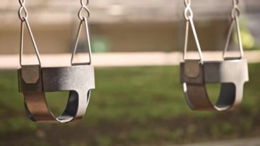 Boş salıncaklar parkta yavaşça hareket ediyor. Yaz güneşli bir gün. Arka planda yeşil ağaçlar var. Kilitlenme. Karantina ve tecrit