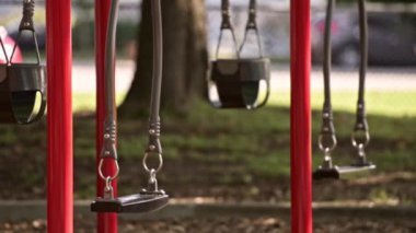 Boş salıncaklar parkta yavaşça hareket ediyor. Yaz güneşli bir gün. Arka planda yeşil ağaçlar var. Kilitlenme. Karantina ve tecrit