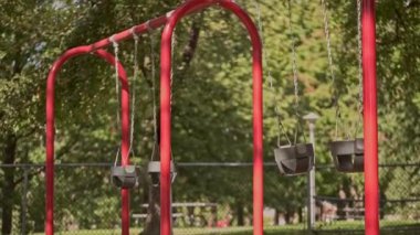 Boş salıncaklar parkta yavaşça hareket ediyor. Yaz güneşli bir gün. Arka planda yeşil ağaçlar var. Kilitlenme. Karantina ve tecrit