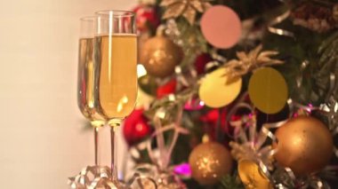 İki kadeh şampanya, şenlikli dekor, sarı ve kırmızı ampullü Noel ağacı süslemesi ve Noel ışıkları.