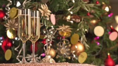 İki kadeh şampanya, şenlikli dekor, sarı ve kırmızı ampullü Noel ağacı süslemesi ve Noel ışıkları.