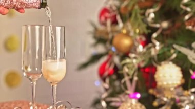 İki kadeh şampanya, şenlikli dekor, sarı ve kırmızı ampullü Noel ağacı süslemesi ve Noel ışıkları.