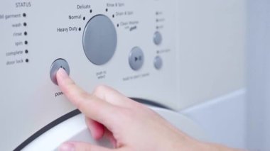 Finger adjusting settings and pressing the start button on washing machine.