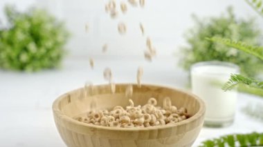 Slow motion of cereal falling into a wooden bowl in a white bright kitchen, close up. Circle shaped whole grain cereals for healthy breakfast.
