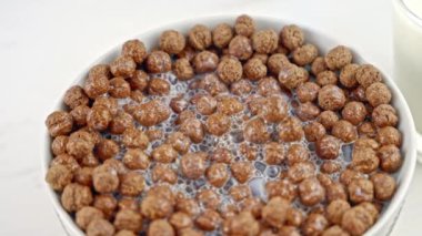 Chocolate cereal with white dairy foam in a white bowl. Cereal with milk for breakfast. Close-up. Slow motion.