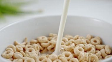 Slow motion close up of pouring and splashing fresh milk into white bowl full of Whole Grain Cereals. Healthy food eating. Round whole grain cereals with milk for healthy breakfast. 
