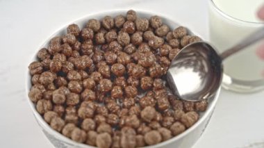 Slow motion of spoon mixing chocolate cereal with milk. Eating cereal with milk for breakfast. Close-up.