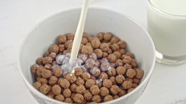 Slow motion, close up of pouring and splashing fresh milk into white bowl full of chocolate cereal.