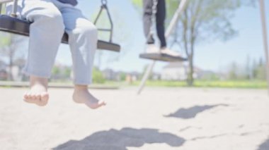 İki kardeş parkta salıncakta sallanıyor. Sevimli yalınayak çocuklar yaz parkında sallanırken eğleniyorlar. Çocukluk eğlence konsepti.