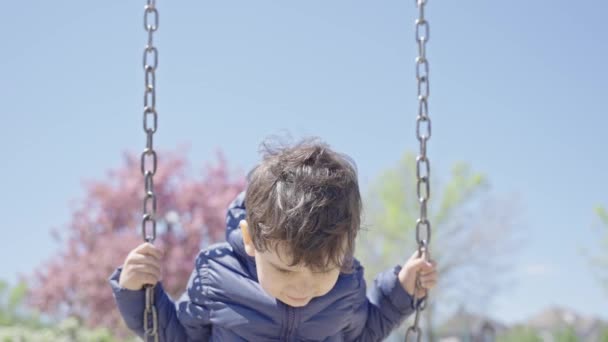 学龄前男孩在公园里荡秋千玩耍 快乐的蹒跚学步的幼儿在春天的操场上荡秋千 童年休闲概念 — 图库视频影像