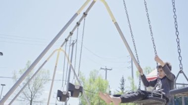 Parkta sallanan yalın ayaklı çocuğun ağır çekimleri. Baharda salıncakta sallanan sevimli çocuk. Boş zaman aktivitesi ve çocukluk konsepti.