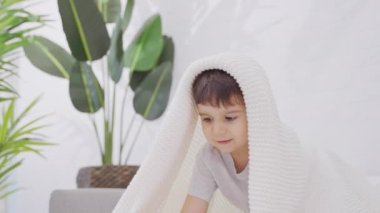 Sevimli çocuk sabahları evde beyaz kapakla eğleniyor. Yavaş Hareket.