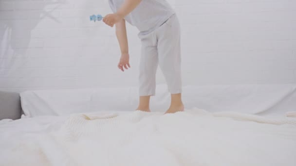 可爱的小男孩 拿着洁白新鲜的床上用品在床上跳得很开心 笑得开心的孩子到处鬼混 在家里玩 慢动作 — 图库视频影像