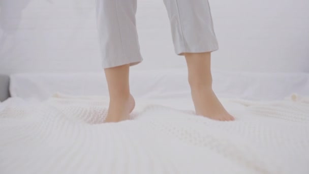 活跃的白人男孩在床上跳 早上腿在白色被褥上跳着 靠在腿上 幸福和自由的概念 慢动作 — 图库视频影像