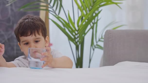 衣冠楚楚的小男孩玩得很开心 在家里喝着一杯清澈的水 健康生活方式的概念 慢动作 — 图库视频影像