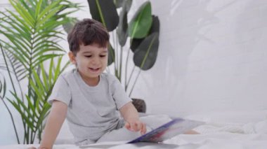 Kafkasyalı şirin bir çocuk bir kitaba bakıyor. Anaokulundaki gülümseyen çocuk masal kitabındaki resimleri seyrediyor. Evdeki yatakta kitap okuyan bir çocuk.. 