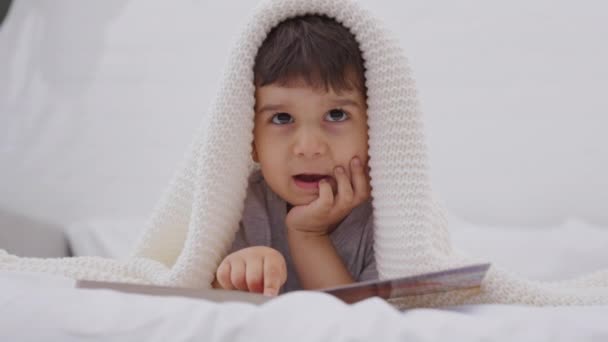 Preschool Kid Lying White Bed Watching Pictures Storybook Looking Camera — Stock Video