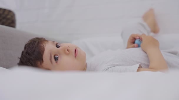 Милий Маленький Хлопчик Прокидається Ліжку Білими Свіжими Постільними Речами Щаслива — стокове відео