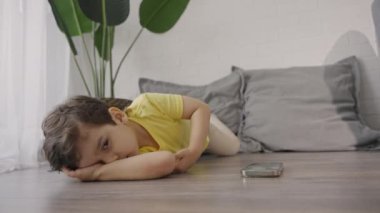 Mobil ekrana bakıp çizgi film izlemekten, cep telefonu kullanmaktan ve online oyunlar oynamaktan, yerde yatmaktan yorgun düşmüş şirin bir çocuk. Modern teknolojiye bağımlılık kavramı 