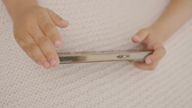 Top view çocuk elleri cep telefonu tutarken çevrimiçi video oyunları oynarken ekrana dokunuyor, evde eğleniyor. Kapalı alanda cep telefonu kullanan modern teknoloji çocuğuna bağımlı.