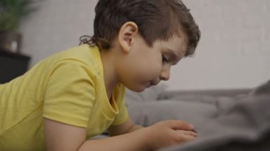 Anaokulu çocuğu mobil ekrana bakıyor, modern cihaz akıllı telefon kullanıyor, sosyal medya uygulamaları izliyor ya da online oyunlar oynuyor, evdeki kanepede oturuyor.. 