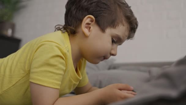 就学前の笑顔の子供の男の子は モバイル画面を見て 現代のガジェットのスマートフォンを使用してお楽しみください ソーシャルメディアアプリを見たり オンラインゲームをプレイ 自宅でソファに座って — ストック動画