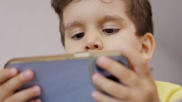 就学前の子供の男の子は モバイル画面を見て 現代のガジェットのスマートフォンを使用してお楽しみください ソーシャルメディアアプリを見たり オンラインゲームをプレイ 自宅でソファに横たわって — ストック動画