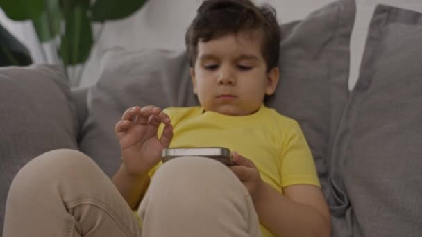 Lille Sød Knægt Slapper Sofaen Ved Hjælp Elektronisk Applikation Smartphone – Stock-video