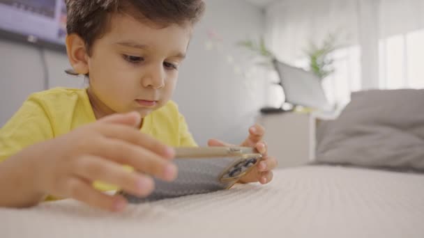 かわいい小さな男の子は 携帯電話を使用して 携帯電話を見て 自宅でスマートフォンでビデオを見るオンラインゲームをプレイ愛らしい幼稚園児 — ストック動画