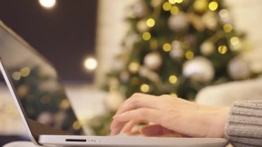 Dizüstü bilgisayarda yazan kadın ellerini, Noel ağacını ve arka planda Noel ışıklarını kapat. Noel boyunca internette çalışan bir kadın. Bilgisayarında, bilgisayarında internette sörf yapan bir kadın..