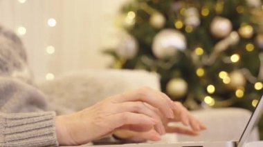 Noel tatilinde evde online çalışan bir kadın. İnternetten Noel alışverişi. Bilgisayarında internette sörf yapan bir kadın. Noel arkaplanında klavyeye yazı yazan eller.
