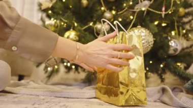 Noel arkaplanında Noel ağacı, ışık ve balolarla süslenmiş bir Noel ağacının altında hediye alan bir kadın.. 