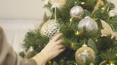 Yeni yıl tatili için modern evde Noel ağacı süsleyen bir kadın. Tatillerde sıcak bir ev. Yavaş çekim. 
