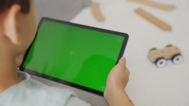 Çocuk oyun oynuyor ya da krom anahtar geçmişi olan bir tablette sosyal medya kullanıyor. Yeşil ekranlı ipad tutan çocuk tahta oyuncak arabayla ilgilenmiyor
