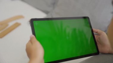 Çocuk sağa sola eğik yeşil ekranlı bir tablet bilgisayar, kenar görünüm.