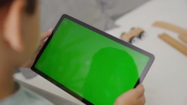 Çocuk sağa sola eğik yeşil ekranlı bir tablet bilgisayar, kenar görünüm.