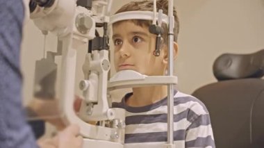 Küçük çocuklar göz muayenesi için göz doktoruna gittiklerinde phoropter kullanmışlar. Doktor elleri phoropter 'i genç çocuğun gözlerine yaklaştırıyor.