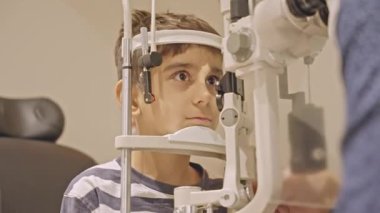 Küçük çocuklar göz muayenesi için göz doktoruna gittiklerinde phoropter kullanmışlar. Doktor elleri phoropter 'i genç çocuğun gözlerine yaklaştırıyor.