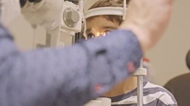 Küçük çocuklar göz muayenesi için göz doktoruna gittiklerinde phoropter kullanmışlar. Doktor elleri phoropter 'i genç çocuğun gözlerine yaklaştırıyor.