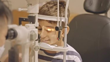 Küçük çocuklar göz muayenesi için göz doktoruna gittiklerinde phoropter kullanmışlar. Doktor elleri phoropter 'i genç çocuğun gözlerine yaklaştırıyor.